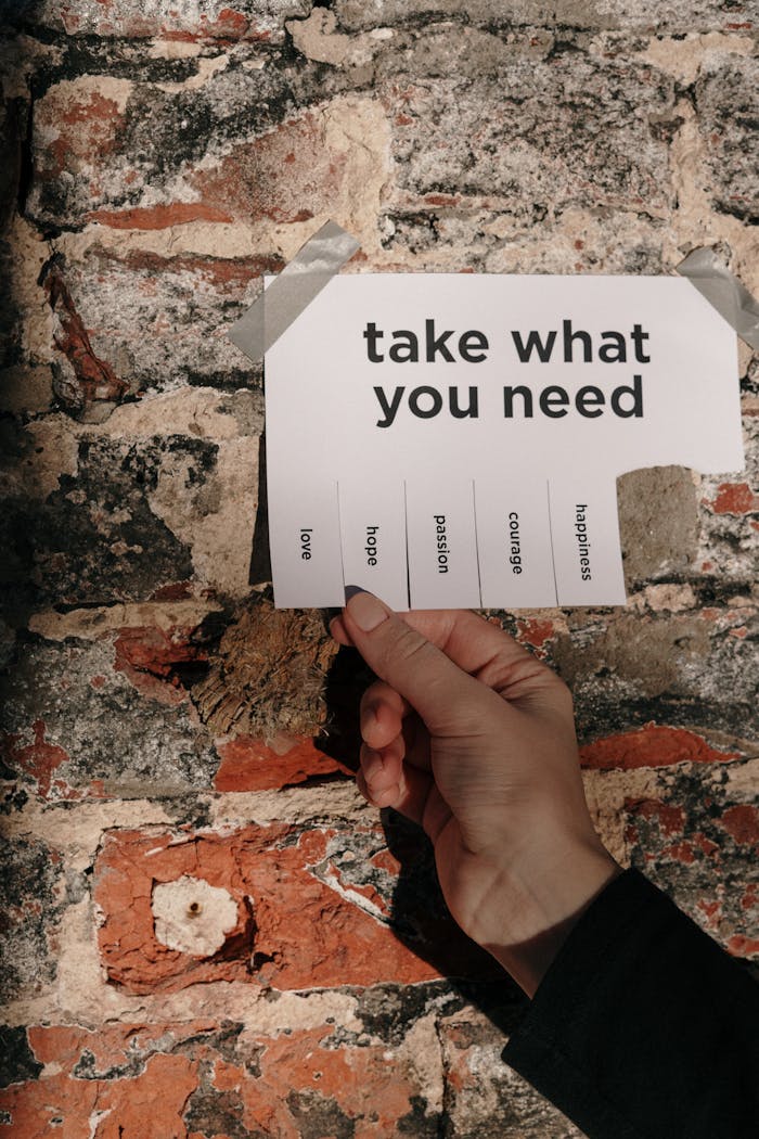 A hand holding a paper note taped on a brick wall with motivational words to pick from.